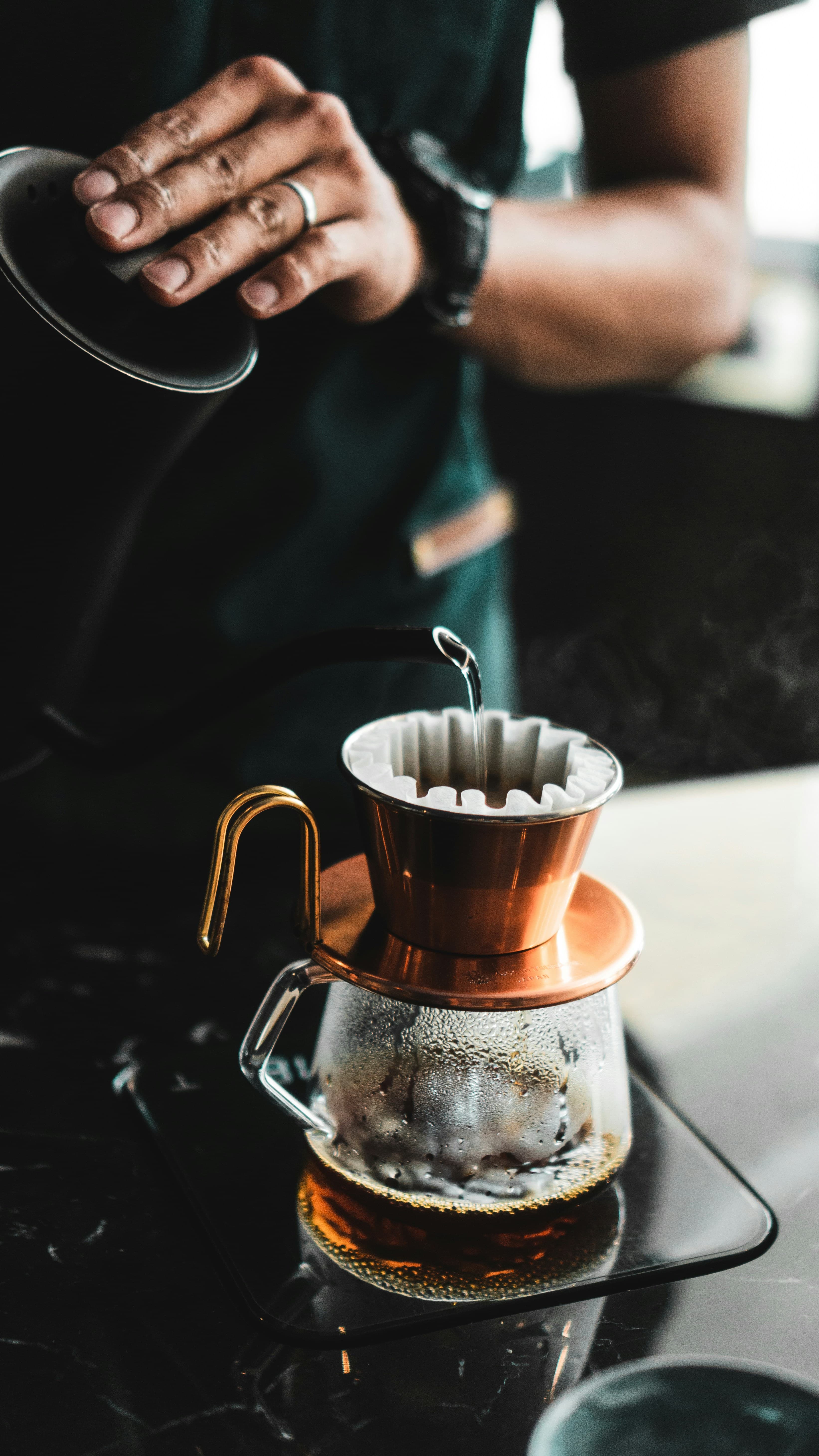 A hand pouring water over coffee in a filter brewer, showing a simple coffee tasting ritual.